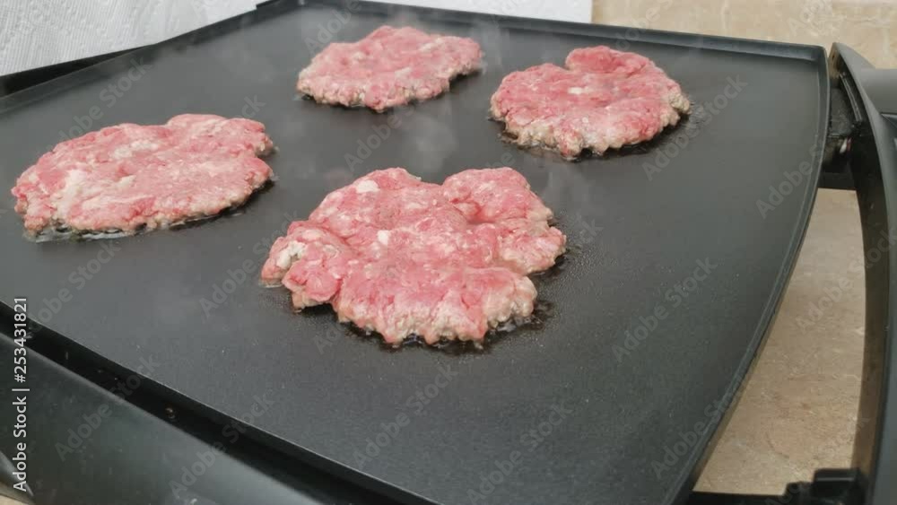 Home cooking - Four hand made burgers from freshly ground beef being grilled on electric griddle from first side. Home cooking - Four hand made burgers from freshly ground beef being grilled on electric griddle from first side.