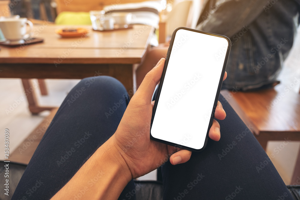 Mockup image of a man's hand holding black mobile phone with blank white screen with woman sitting in cafe Mockup image of a man's hand holding black mobile phone with blank white screen with woman sitting in cafe