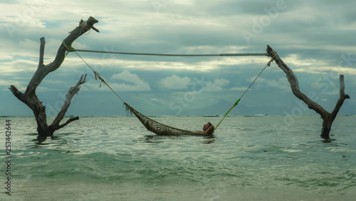 man lying relaxed and happy in sea hammock amazing set up on tree trunks at tropical island beach in relaxing holidays travel getaway and tourist destination