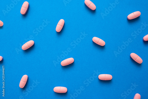 A lot of pink pills on blue background texture close up.