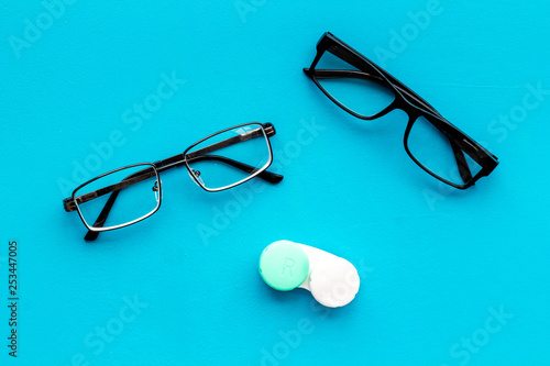 Eye problems. Glasses with transparent lenses and contact lenses on blue background top view