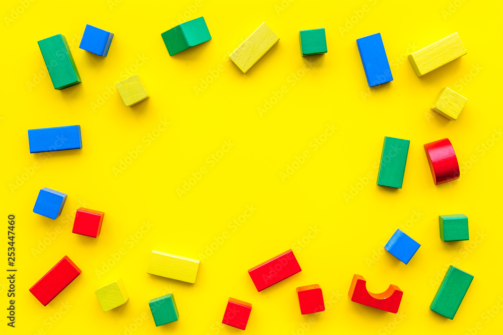 Obraz premium Construction game for kids. Wooden building blocks, toy bricks on yellow background top view space for text frame