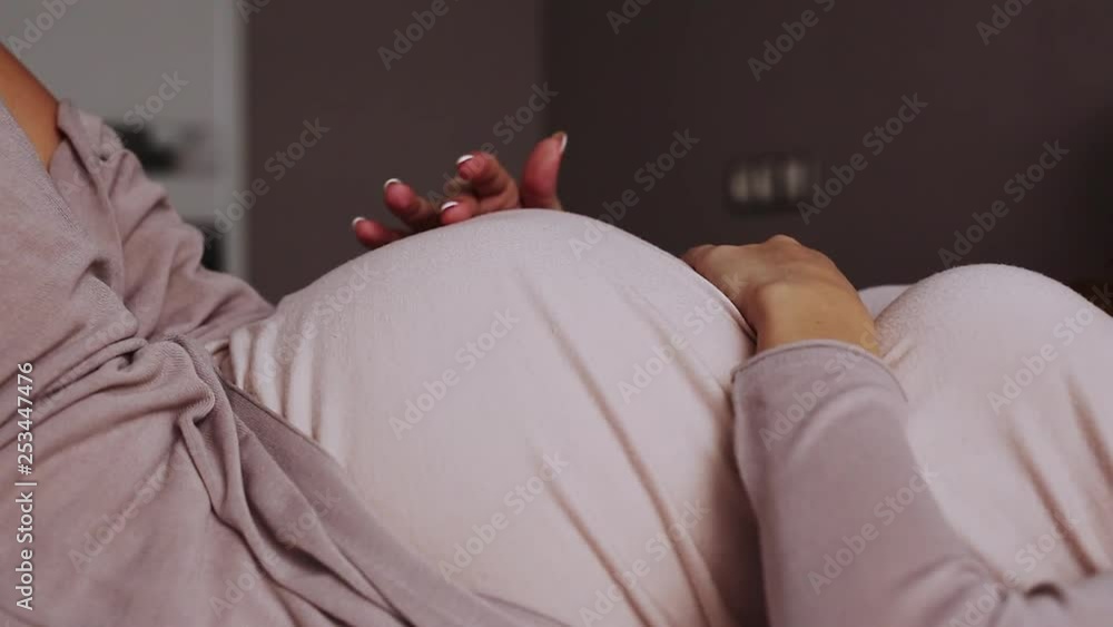 Pregnant woman feels her future baby pushing on a bed at home - Front View
