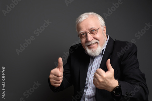 business, white-haired man in glasses on a gray background smiles and shows approval