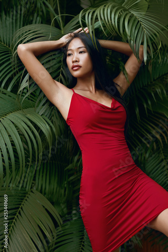 Fashion. Woman model in red dress with green palm leaves