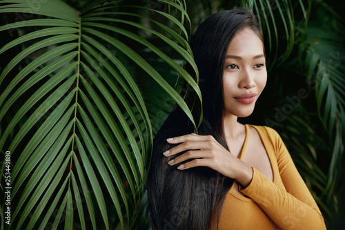 Hair beauty. Woman model with long straight hair in palm leaves photo