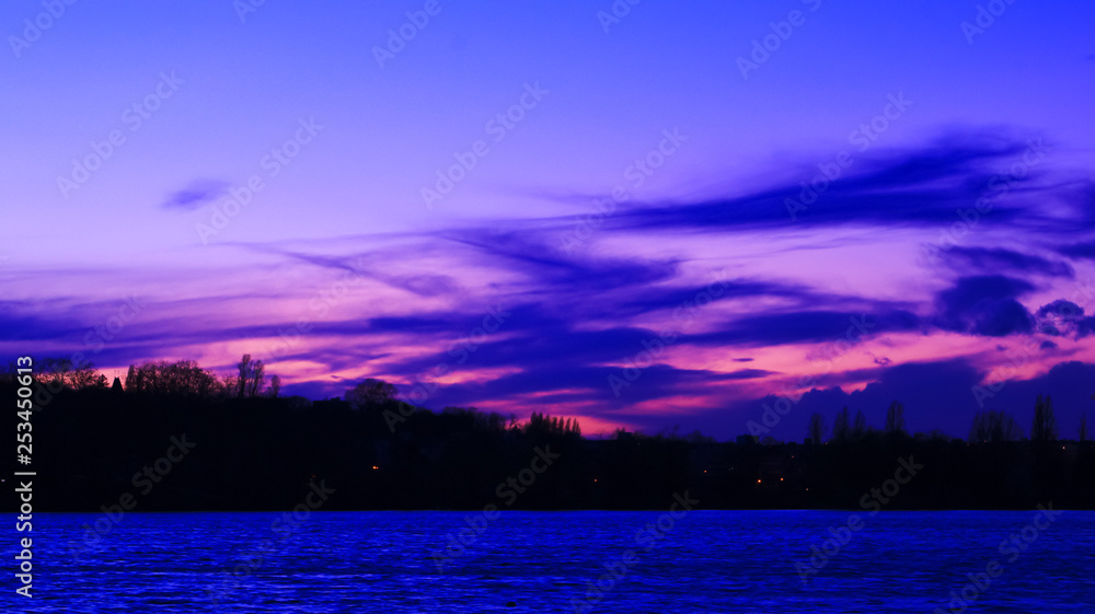 Blue and pink clouds in the distance above the sea. Very colorful sunset over a forest at the foot of the water
