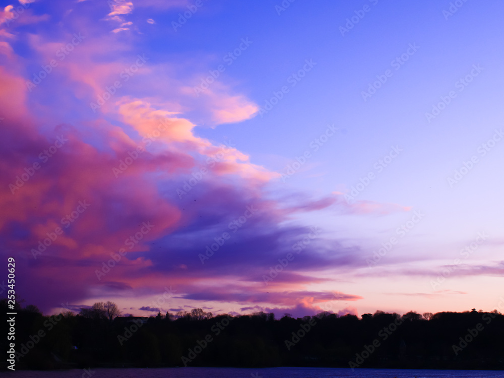 Big pink cloud coming over trees and lake in the countryside. Clouds threatening rose at sunset Big pink cloud coming over trees and lake in the countryside. Clouds threatening rose at sunset