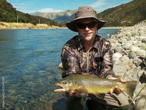 a fly fisherman poses with a large live new zealand brown trout
