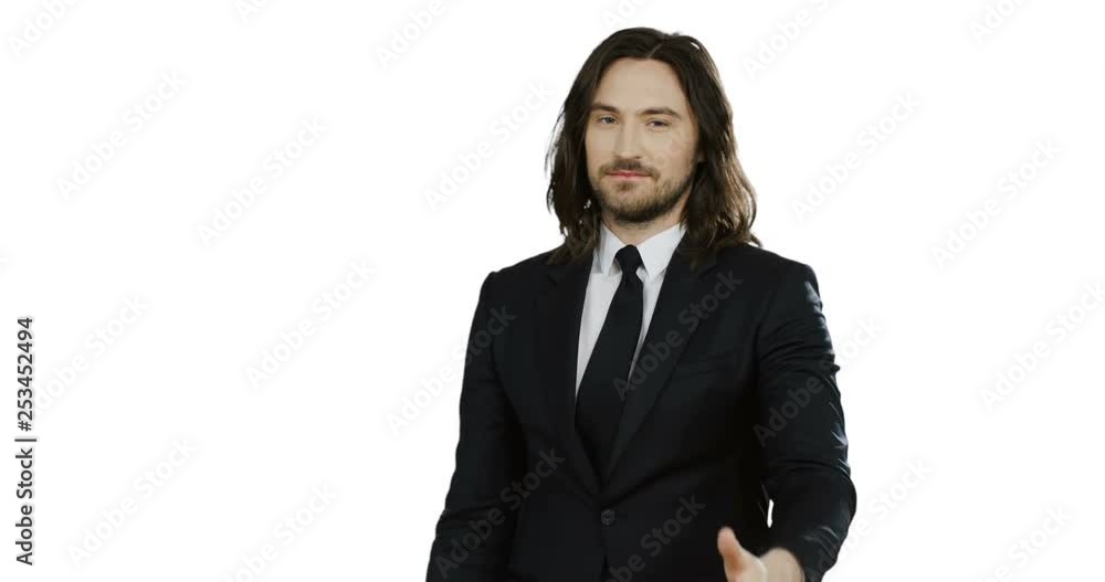 Young attractive man in the suit and tie standing in front of the camera, smiling and giving his thumb up. White wall back. Young attractive man in the suit and tie standing in front of the camera, smiling and giving his thumb up. White wall back.