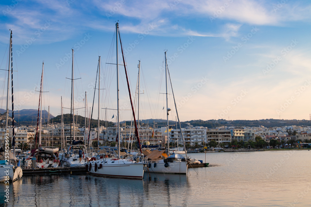 Fototapeta premium Beautiful cityscape port, arsenal, modern buildings, yachts, azure sea water on the background of stormy sky at evening, harbour of Rethymno, island of Crete, Greece, Southern Europe.