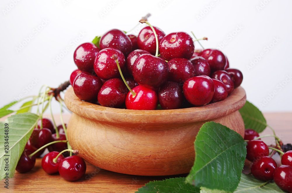 Sweet cherry fruits with leaves in a wooden bowl Sweet cherry fruits with leaves in a wooden bowl