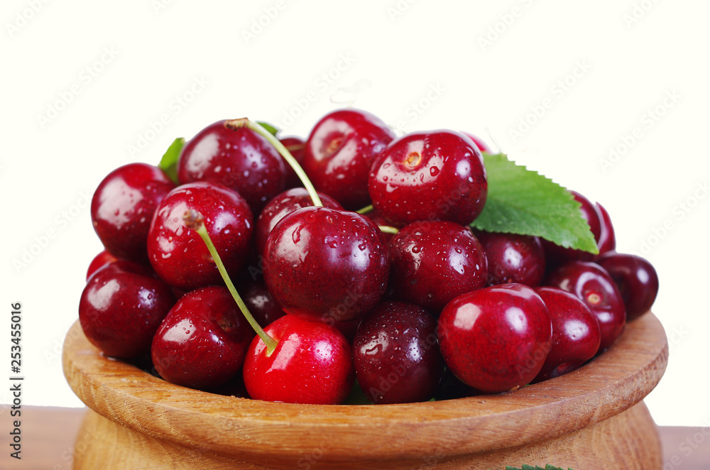 Sweet cherry fruits with leaves in a wooden bowl on a white background Sweet cherry fruits with leaves in a wooden bowl on a white background