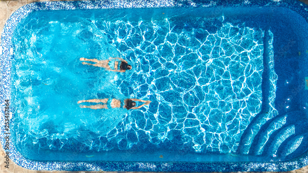 Active girls in swimming pool water aerial drone view from above, children swim, kids have fun on tropical family vacation, holiday resort concept
