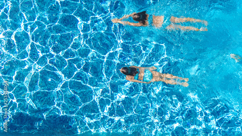 Active girls in swimming pool water aerial drone view from above, children swim, kids have fun on tropical family vacation, holiday resort concept