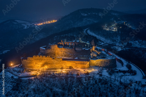 Visegrad, Hungary - Aerial view of the beautiful, illuminated high castle of Visegrad at blue hour with snowy hills of Pilis on a winter night
