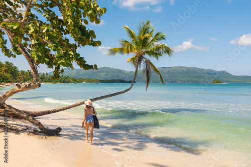 Attractive girl in bikini and hat walk on beach under the palm tree in Las Galeras. © Mihailo