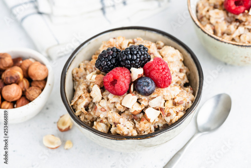 Oatmeal porridge with fresh berries and nuts in bowl on white background. Closeup view. Healthy breakfast food, healthy eating, dieting, weight loss concept
