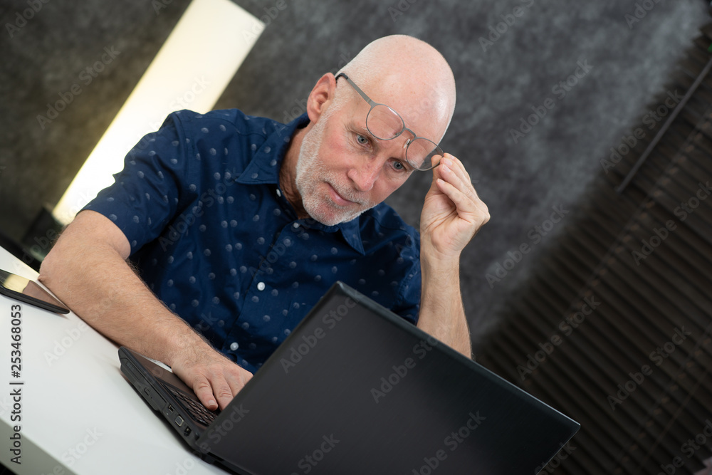 Senior businessman using laptop, he is having difficulties and vision problems Senior businessman using laptop, he is having difficulties and vision problems