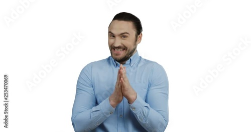 Handsome cheerful young man in the blue shirt standing on the white screen background, smiling archly while rubbing his hands. photo