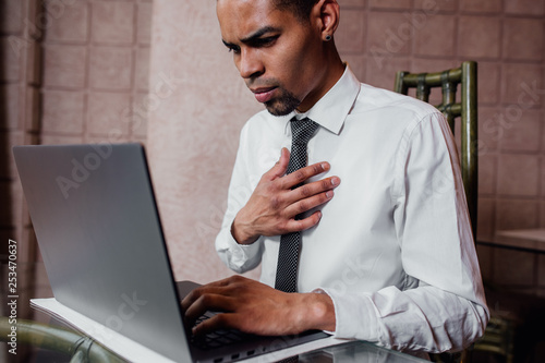 african american man making a mistake, stunned and speechless or seeing something he shouldnt see, laptop, dressed in white shirt, close up, indoor, negative human emotion facial photo