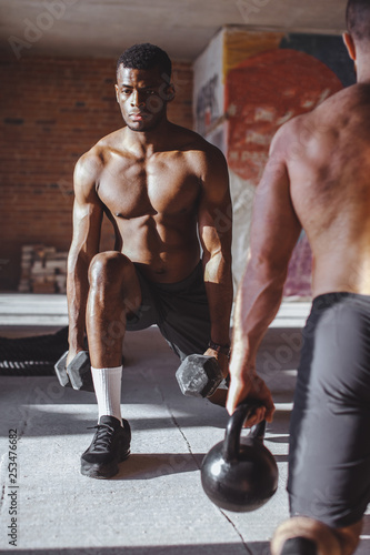 Focused male african and caucasian athletes showing determination and endurance exercising legs and back musculs during body core crossfit workout photo