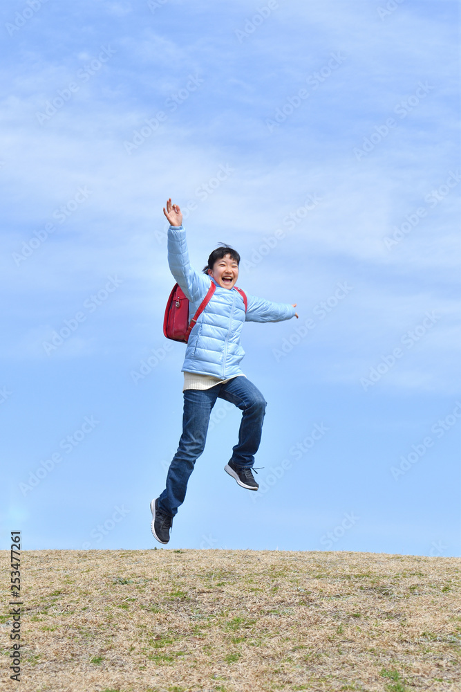 Japanese elementary school girl jumping  in the blue sky