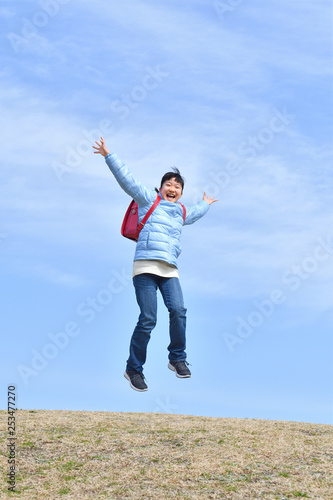 Japanese elementary school girl jumping in the blue sky