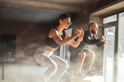 Fit caucasian couple doing squats on boxes in a crossfit style gym, well lit by bright sunlight. photo