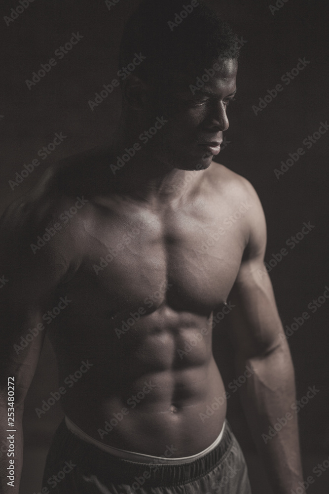 Toned image of strong afroamerican athletic man with naked perfect shape musculs standing isolated over dark background. Toned image of strong afroamerican athletic man with naked perfect shape musculs standing isolated over dark background.