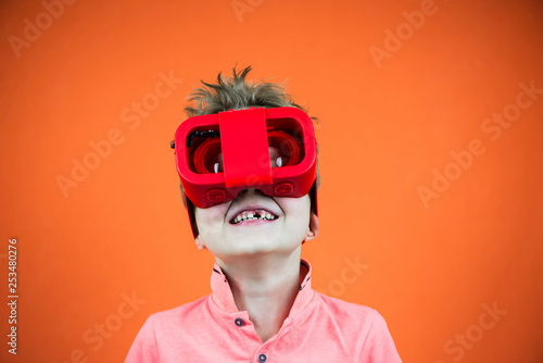 funny boy plays in glasses of virtual reality for the phone on a bright orange background