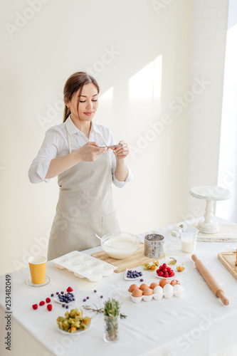 pleasant girl using her smart phone while cooking a dessert, close up photo.spare time, copy space