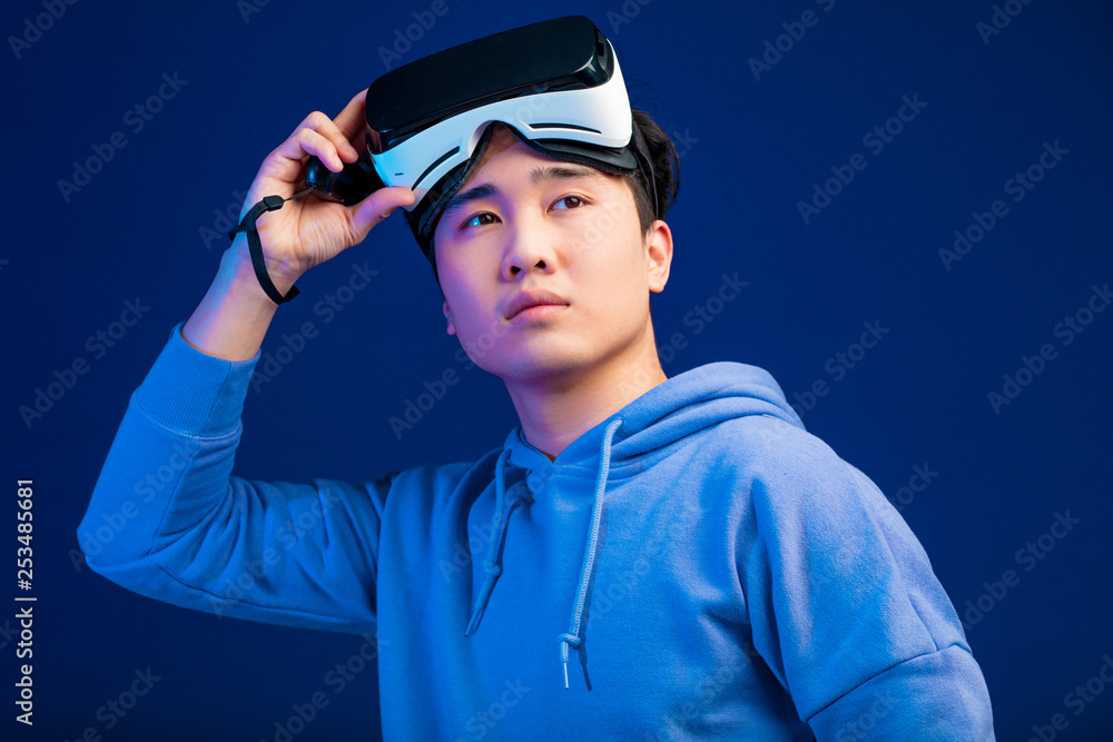 3d technology, virtual reality, gaming, entertainment and people concept - handsome young Asian male video gamer, taking off his virtual reality headset from eyes and looking aside into space. Poster 3d technology, virtual reality, gaming, entertainment and people concept - handsome young Asian male video gamer, taking off his virtual reality headset from eyes and looking aside into space. Poster