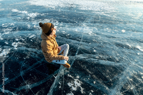 Tourist traveler meditates sitting in Lotus position on the ice of lake Baikal
