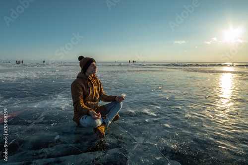 Tourist with a backpack meditates sitting in Lotus position on the ice of lake Baikal. Relaxation and freedom of nature