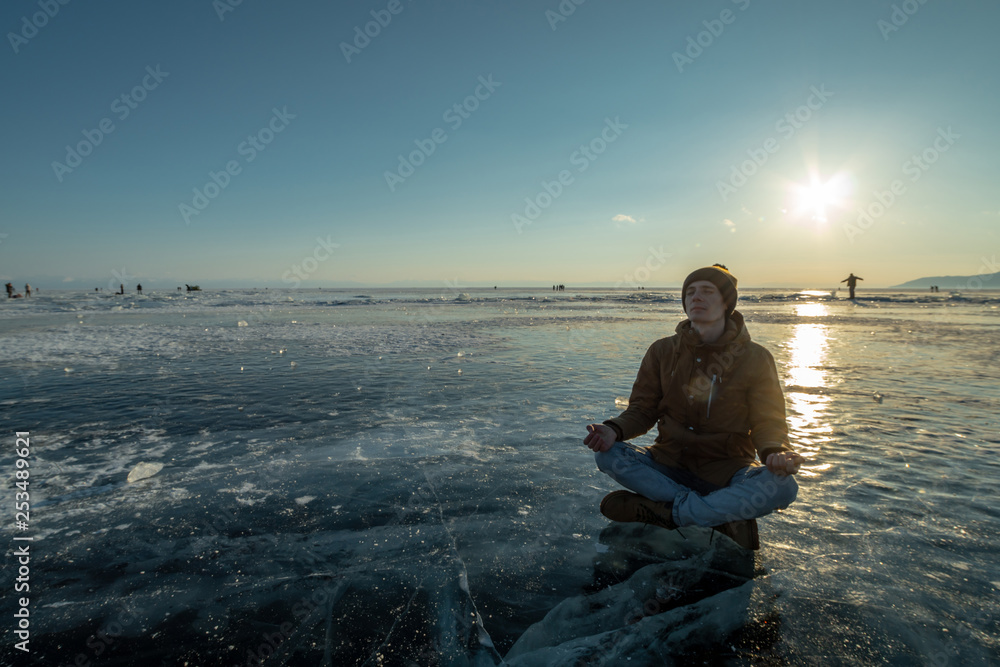 Tourist with a backpack meditates sitting in Lotus position on the ice of lake Baikal. Calm and freedom of nature