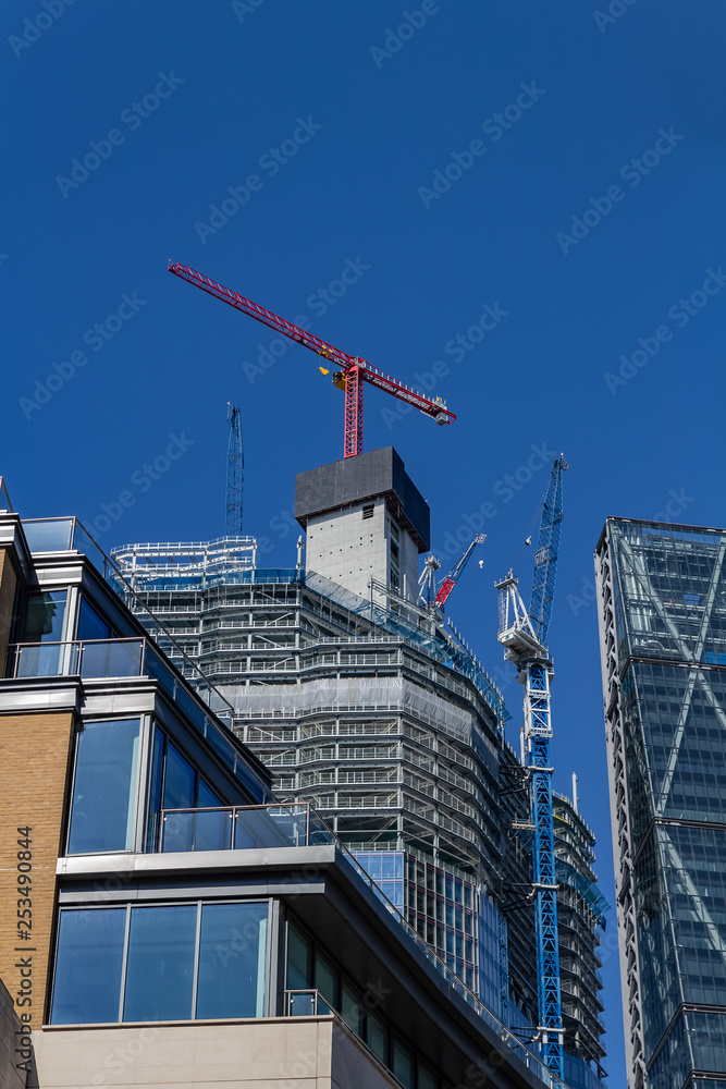 Modern building under construction at a bright sunny day on the blue sky background. Low angle view Modern building under construction at a bright sunny day on the blue sky background. Low angle view