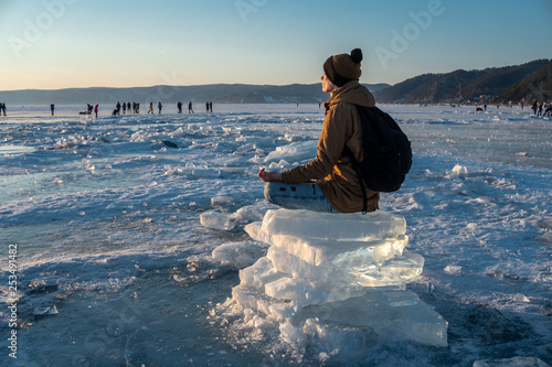 Tourist with a backpack meditates sitting in Lotus position on the ice of lake Baikal