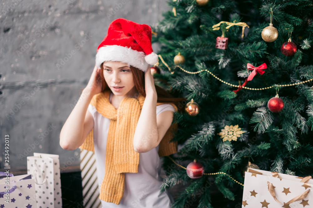 attractive girl putting on a Christmas hat while sitting on the floor, close up photo. copy space, sexy pleasant pensive girl tries a hat while sitting in front of the tree attractive girl putting on a Christmas hat while sitting on the floor, close up photo. copy space, sexy pleasant pensive girl tries a hat while sitting in front of the tree