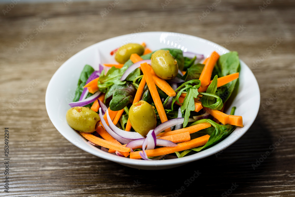 Freshly made vegetable salad with carrot, olives, spinach and onion in a bowl on wooden background. Freshly made vegetable salad with carrot, olives, spinach and onion in a bowl on wooden background.