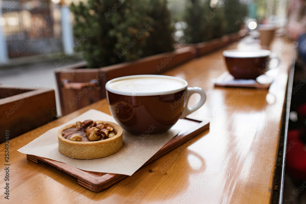 Fototapeta premium two cups of coffee cappuccino with baked dessert on wooden table cappucino on wooden table and girl defocussed on the background cappucino with baked dessert on wooden table