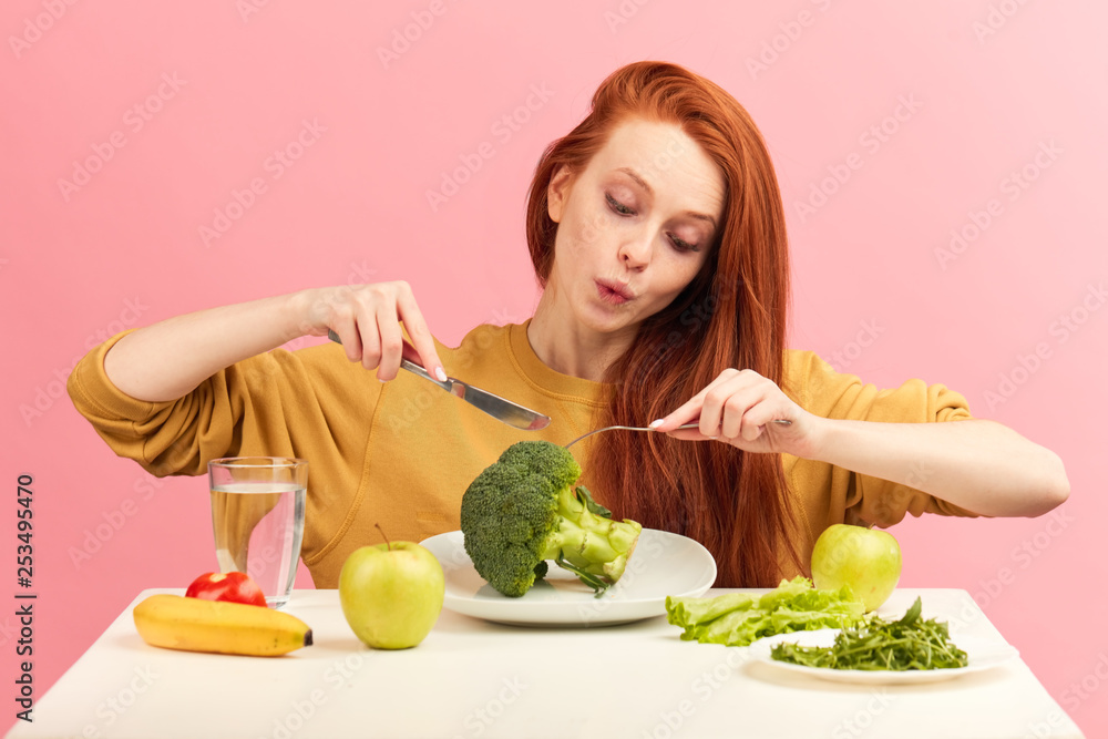 Young beautiful happy attractive female with gorgeous long ginger hair having dinner with fresh broccoli and vegetables at table, isolated over pink background. Healthy diet concept. Vegetarian food Stock Photo | Adobe Young beautiful happy attractive female with gorgeous long ginger hair having dinner with fresh broccoli and vegetables at table, isolated over pink background. Healthy diet concept. Vegetarian food Stock Photo | Adobe