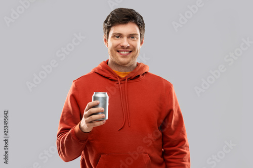 drinks and people concept - happy young man in red hoodie drinking soda from tin can over grey background photo