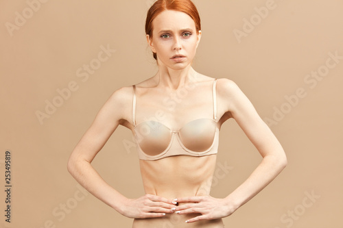 Skinny suffering female in nude underwear tied her waist with measuring tape posing over anorexia and eating disorders