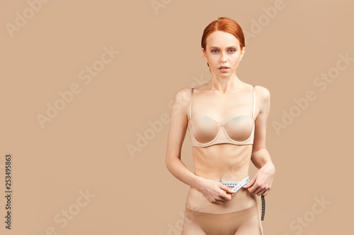 Caucasian female model measuring waist with tape during her weightloss diet, showing perfect results of low calories nutrition but getting unhealthy sick look and eating disorder