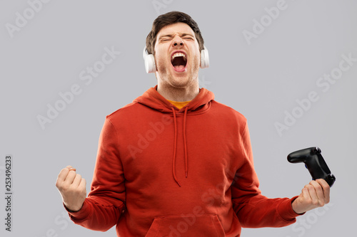 technology, gaming and people concept - happy young man or gamer in headphones with gamepad winning in video game photo