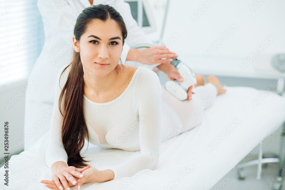 Portrait of brunette woman dressed in white LPG slimming bodysuit, looking at camera while getting lpg integral massage, which is carried out by the latest generation of devices - lpg integral. Portrait of brunette woman dressed in white LPG slimming bodysuit, looking at camera while getting lpg integral massage, which is carried out by the latest generation of devices - lpg integral.