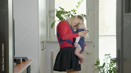A young pretty mom is carrying her little boy in a baby carrier.