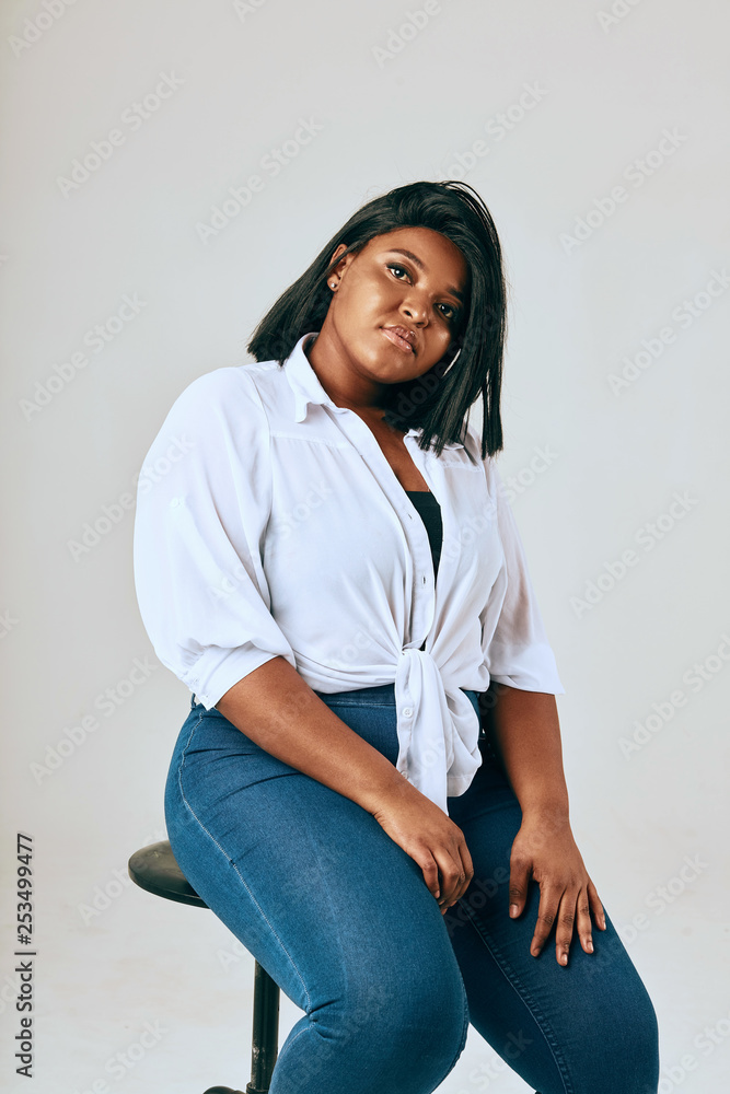 Studio portrait of Plus size african confident female model in white shirt  and jeans, looking at camera posing isolated over white background. Stock  写真 | Adobe Stock