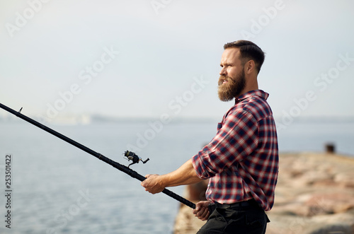 leisure and people concept - bearded fisherman with fishing rod on pier at sea